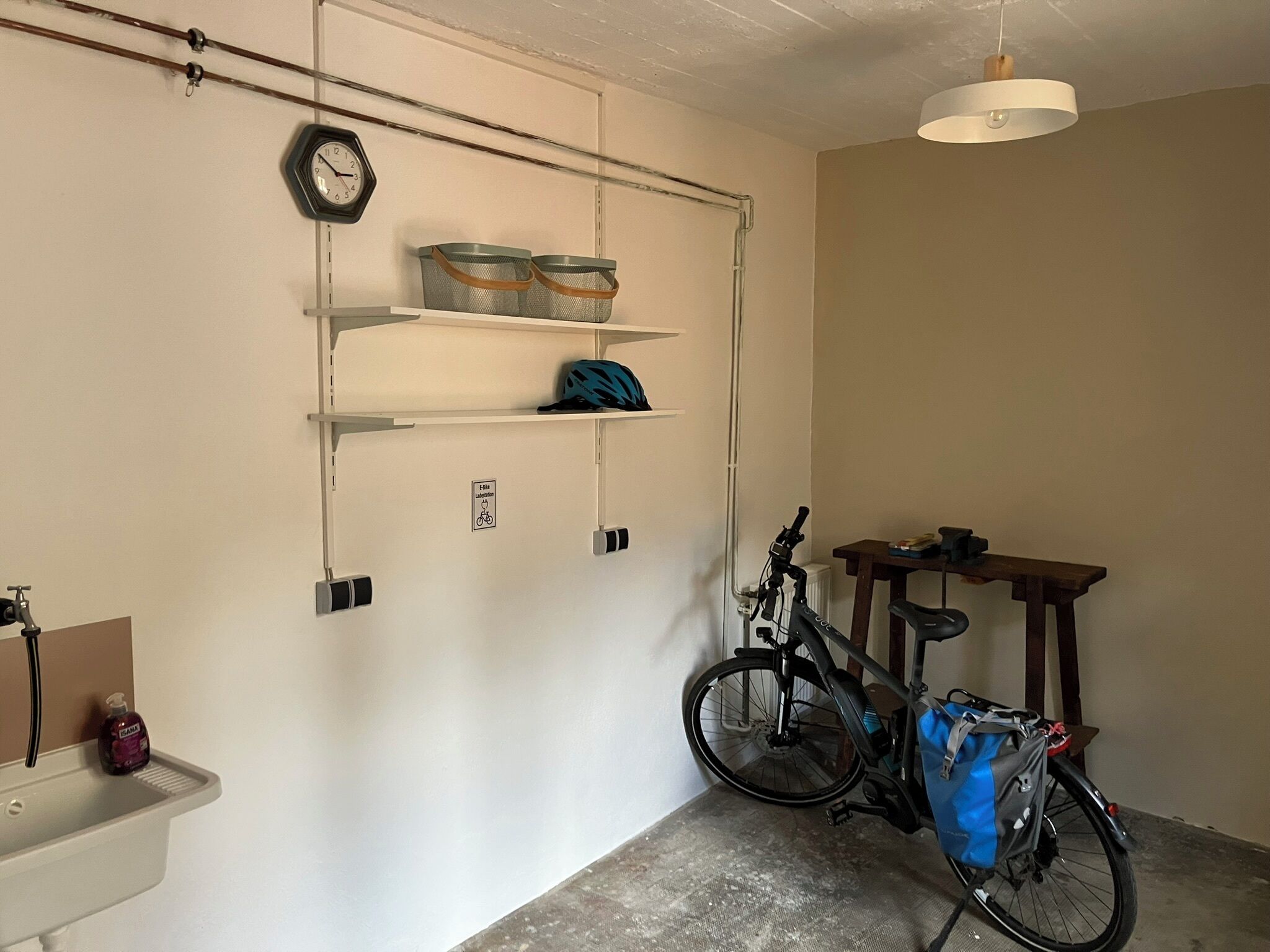 Une pièce avec un vélo, un lavabo, des étagères avec des paniers et une horloge au mur.