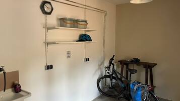 Een kamer met een fiets, een wastafel, planken met manden, en een klok aan de muur.