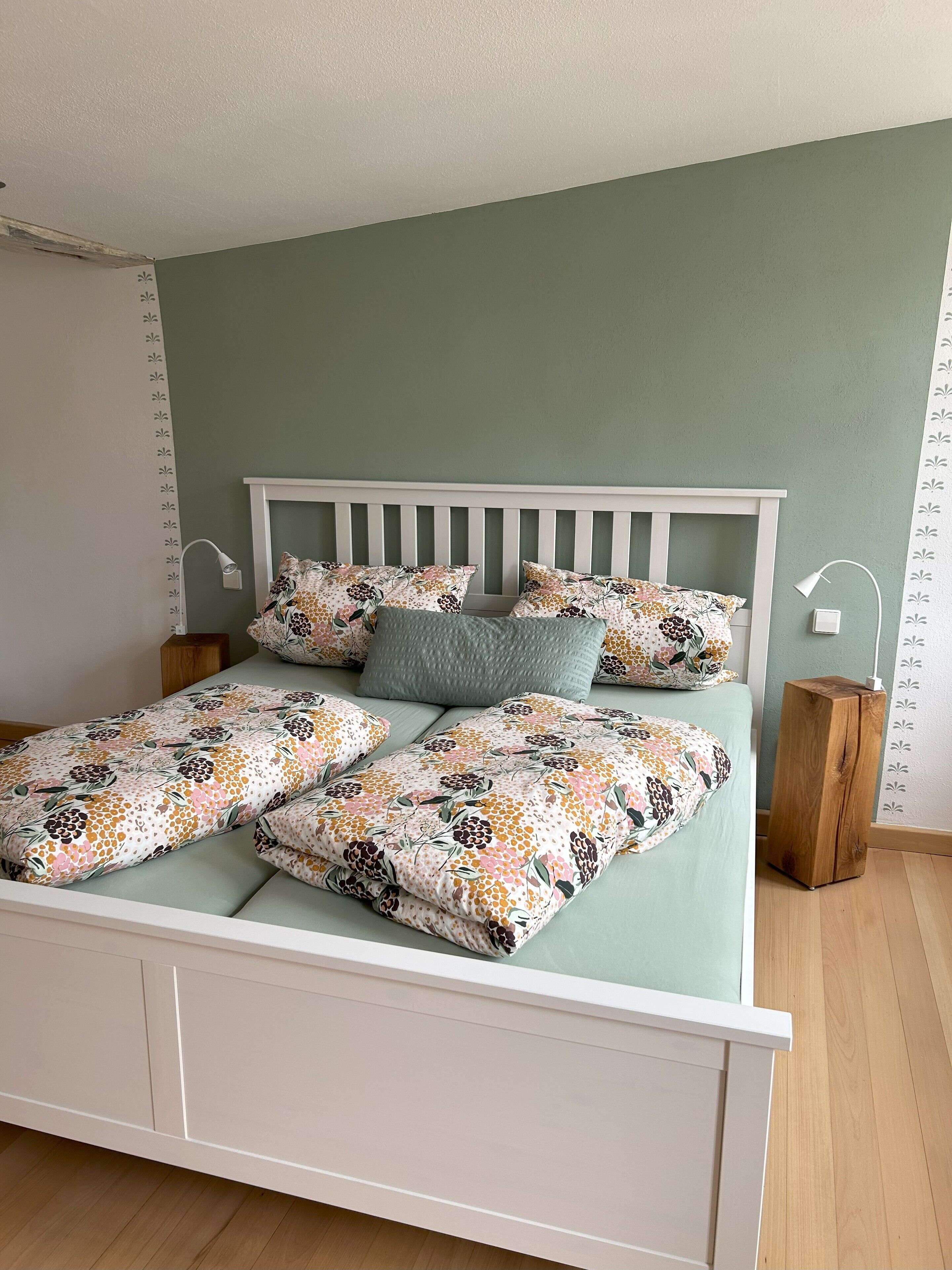 A neatly made bed with floral bedding, a white headboard, and two bedside lamps.
