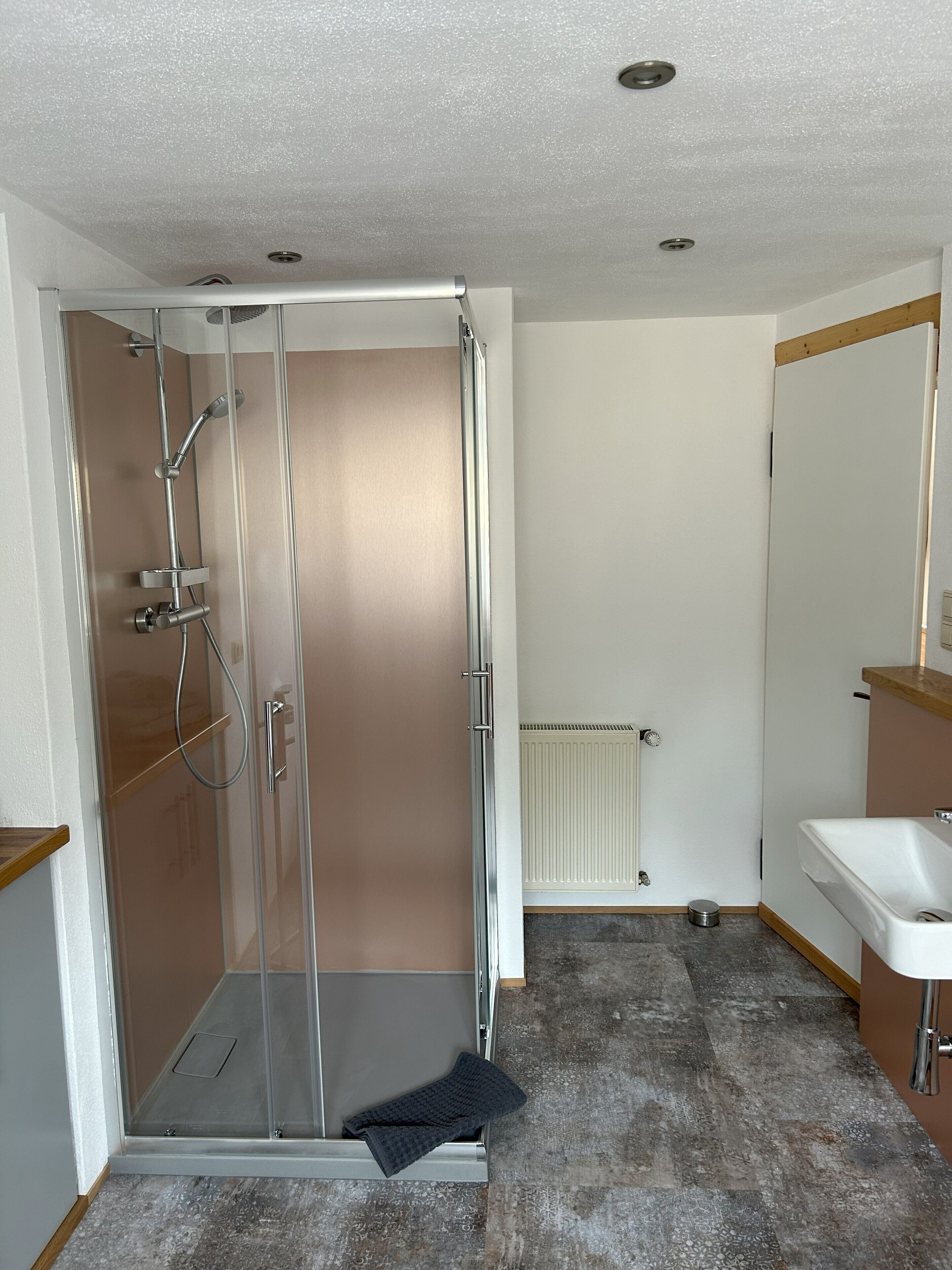 Ein modernes Badezimmer mit Duschkabine aus Glas, einem weißen Waschbecken und einem Heizkörper.