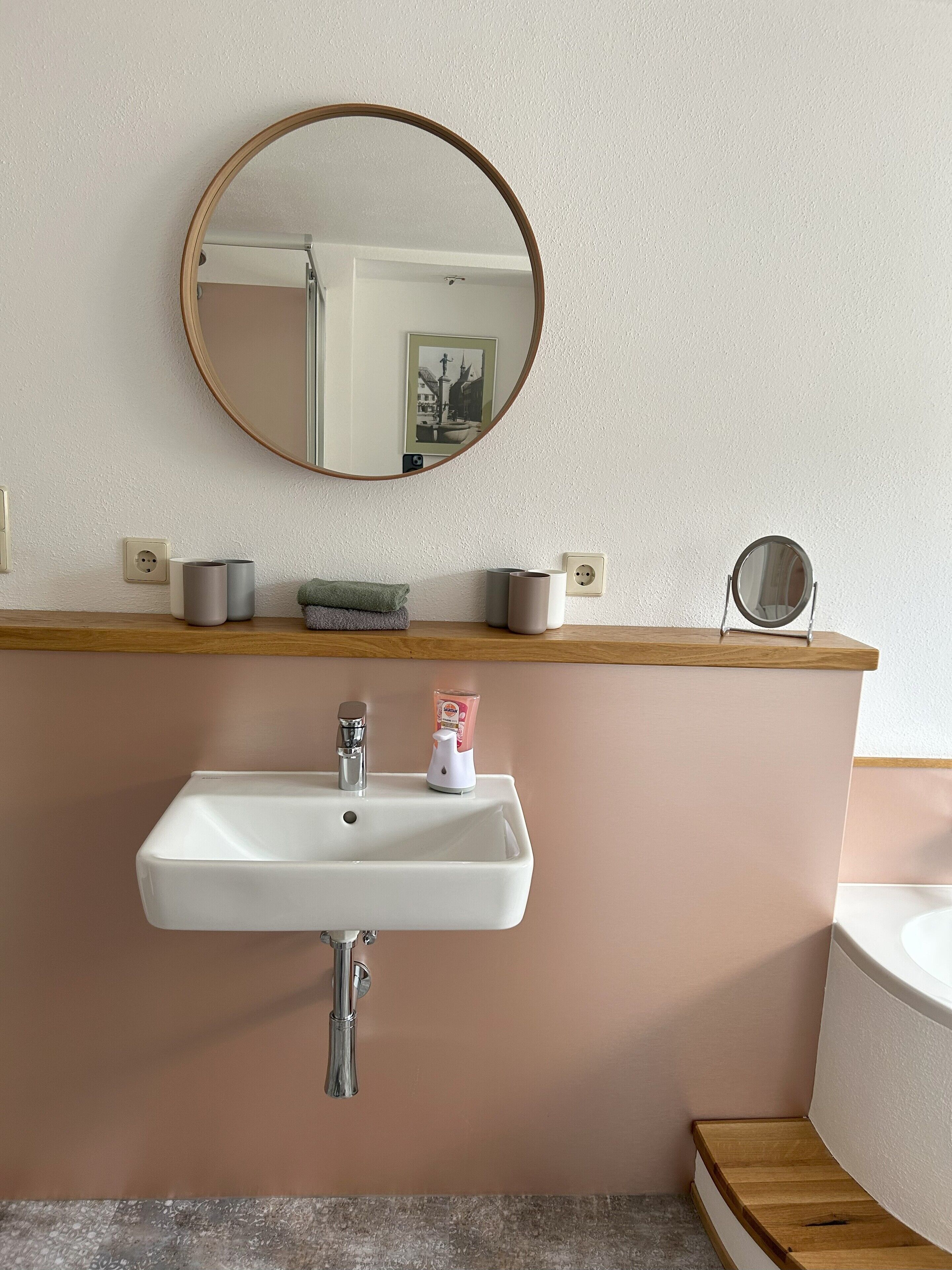 A bathroom with a white sink, a mirror, and a wooden vanity.