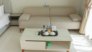 Een moderne hotelkamer met een beige bank, een witte salontafel met voorzieningen, en een klein bijzettafeltje.