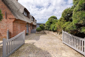 A brick building with a thatched roof, a cobblestone driveway, and a stone wall.