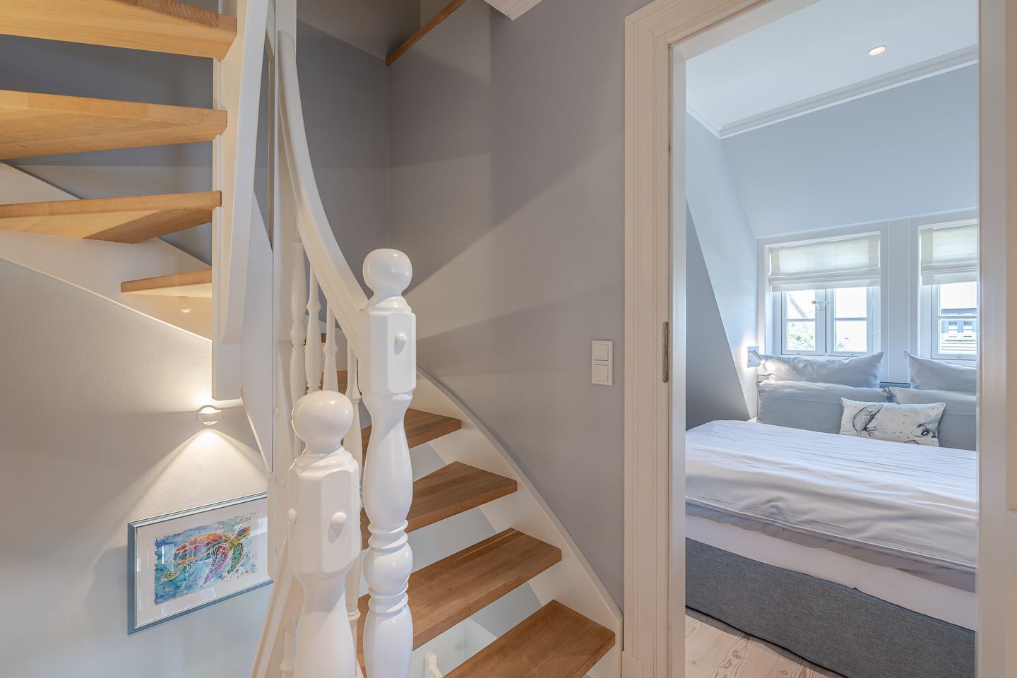 A staircase with white balusters and wooden steps leading to a bedroom with a bed and a window.