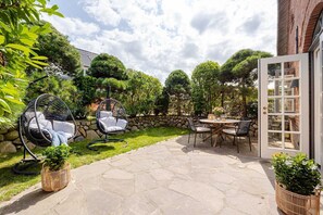 Eine Terrasse mit Steinboden, einem runden Tisch mit Stühlen und zwei Hängesesseln.