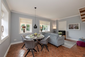 A modern living room with a grey sofa, a dining table with chairs, a TV, and artwork on the wall.