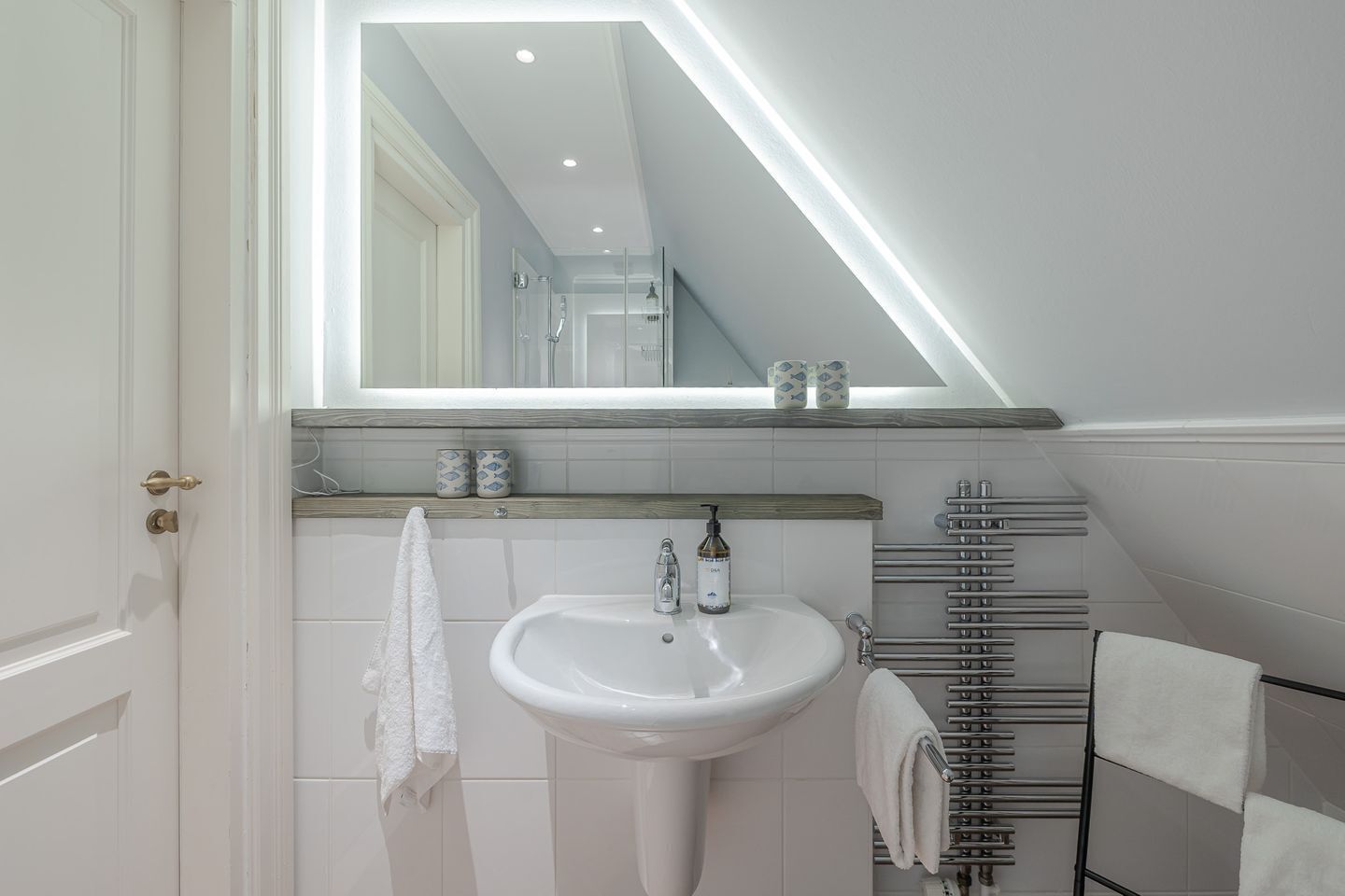 A modern bathroom with a white pedestal sink, a large mirror, and a towel rack.