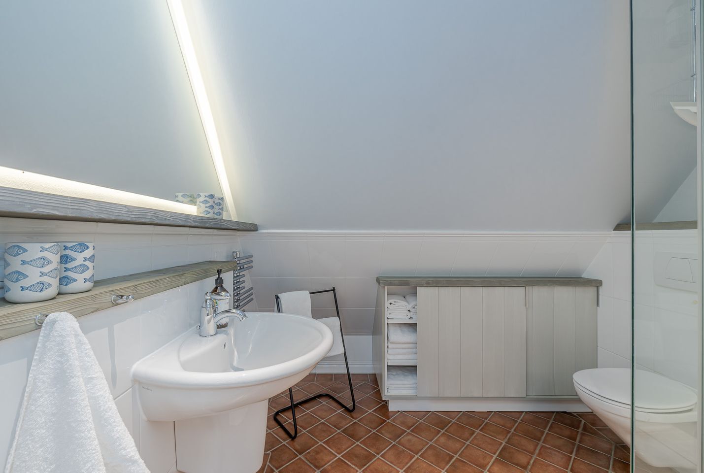 Ein Badezimmer mit einem weißen Waschbecken, einem Spiegel, einem Handtuchhalter und einer Toilette.
