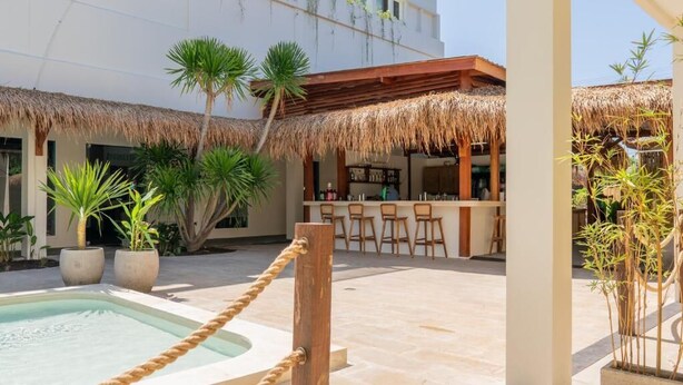 Un espace piscine délimité par une barrière en corde, un bar avec des tabourets et des plantes en pot.