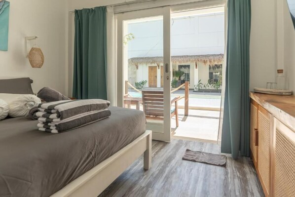 Una camera da letto con un letto, pavimento in legno, vista su uno spazio esterno con una sedia e un tavolo, e una porta che dà sull'esterno.