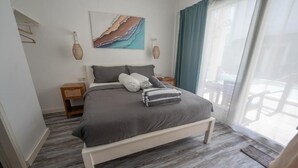 Une chambre à coucher avec un lit, des tables de chevet, un tableau et une vue sur l’extérieur.