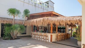 Un espace bar doté d’un toit de chaume, de tabourets de bar en bois et d’un comptoir où se tient le barman.