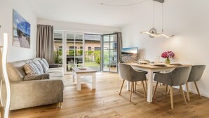 A modern living room with a sofa, a dining table with chairs, and a large sliding glass door leading to a garden.