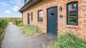 A brick building with a dark door, windows, and a paved walkway.