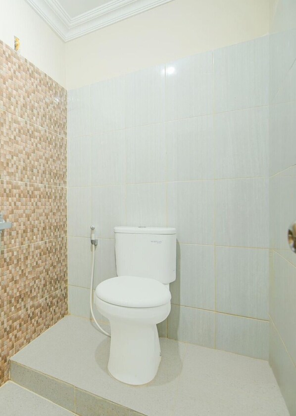 A bathroom with a white toilet, a shower area with a tiled wall, and a tiled floor.