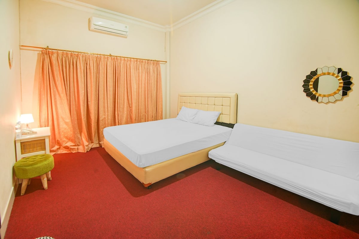 Une chambre avec deux lits, une moquette rouge, un climatiseur, une lampe et un miroir mural.
