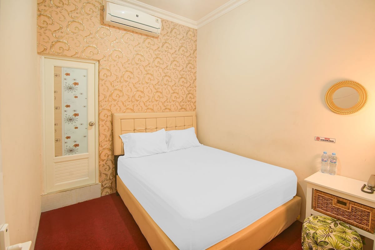 Une chambre à coucher bien rangée, avec un lit, une armoire, une table de chevet avec un miroir et un climatiseur fixé au mur.