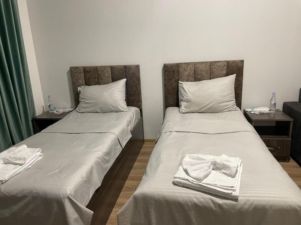 Two single beds with headboards, a wooden floor, a green curtain, and a nightstand with a bottle and glasses.