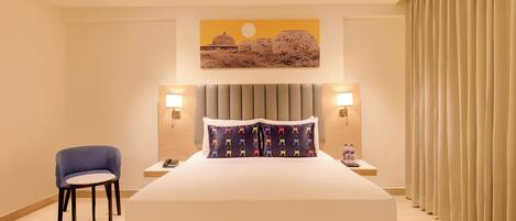 A hotel room with a large bed, two bedside lamps, a chair, a nightstand, and a wall-mounted artwork.