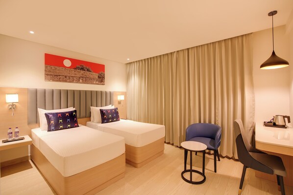 A hotel room with two beds, a desk, a chair, a lamp, and a large window with curtains. - Keys Lite by Lemon Tree Hotels Krishna (Vijayawada)