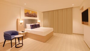 A modern hotel room with a large bed, a desk with a chair, a flat-screen TV, and a painting on the wall. - Keys Lite by Lemon Tree Hotels Krishna (Vijayawada)