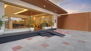 A modern building with a glass facade, outdoor seating area, and a wooden fence. - Keys Lite by Lemon Tree Hotels Krishna (Vijayawada)