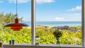 A room with a large window overlooking a coastal landscape with houses and the sea.