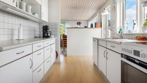 A modern kitchen with white cabinetry, a wooden floor, and a large window providing natural light.