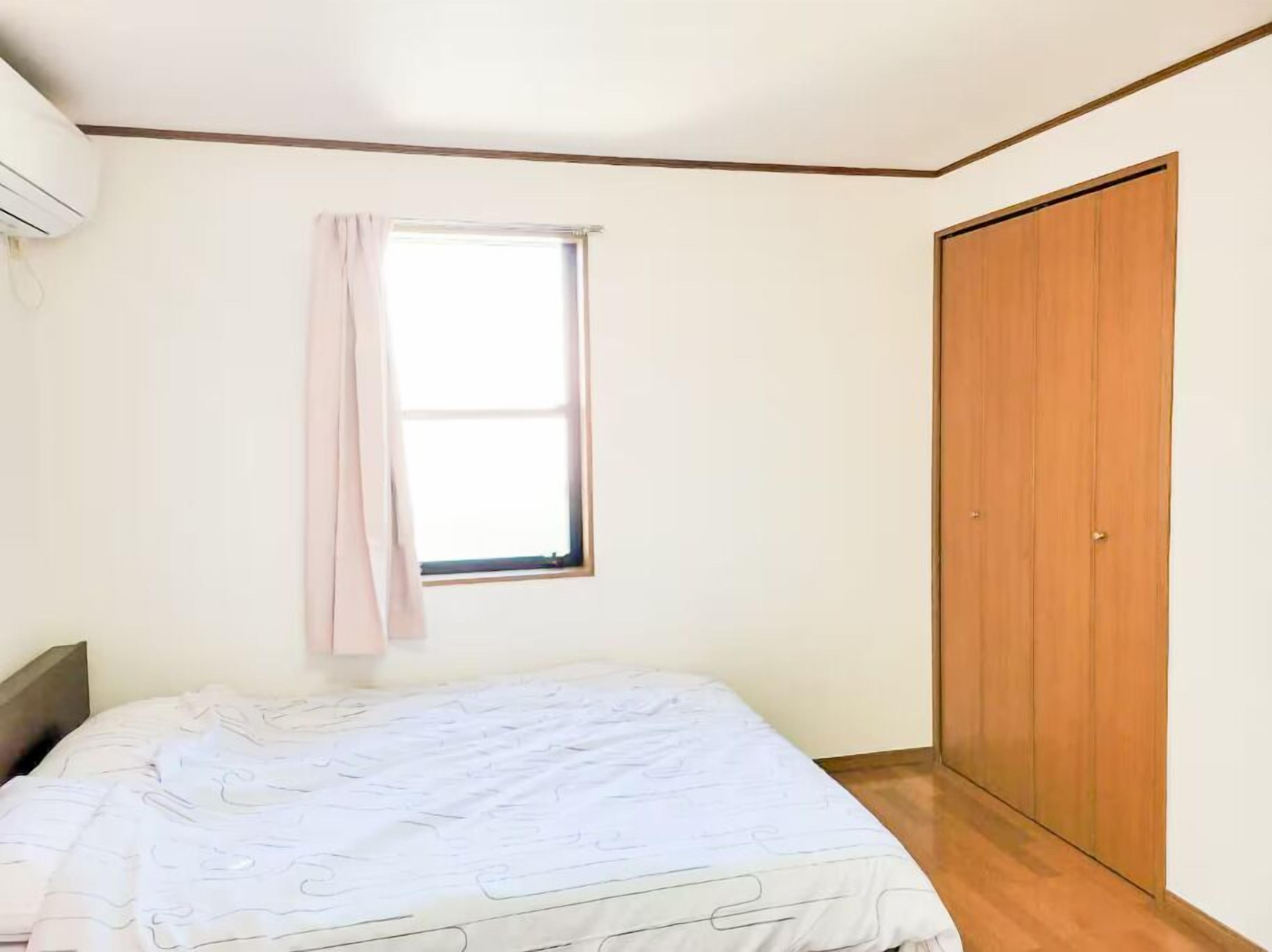 A bedroom with a bed, a window with a curtain, and a wooden wardrobe.