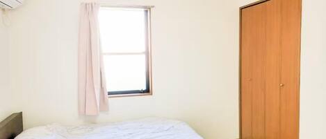 A bedroom with a bed, a window with a curtain, and a wooden wardrobe.
