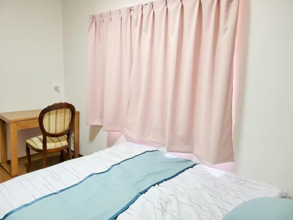Un dormitorio con cama, una silla, un escritorio y una ventana con cortinas.