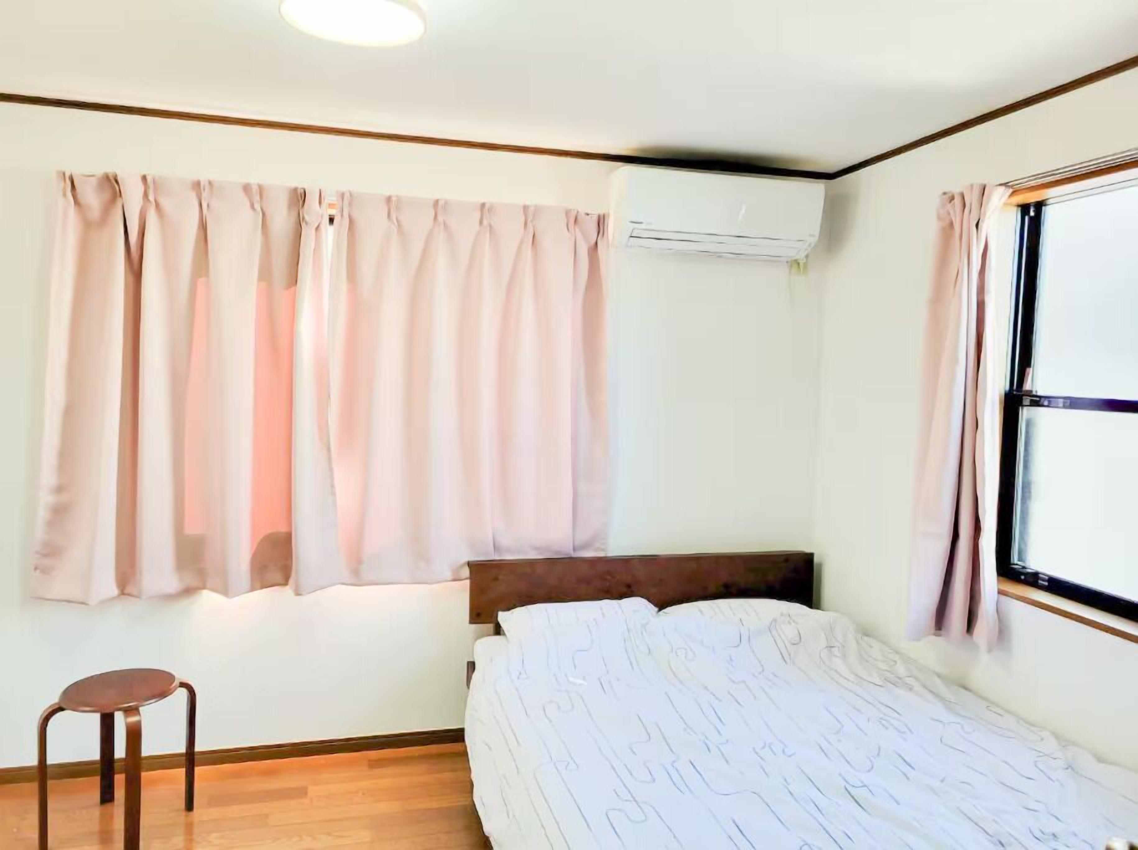 A bedroom with a bed, a wooden headboard, a small stool, and an air conditioning unit.
