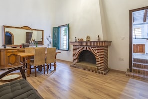 Een eethoek met een houten tafel en stoelen, een open haard, een grote spiegel, en een deur naar een andere kamer.