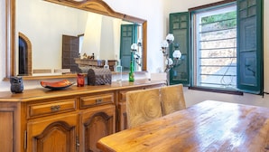 A wooden dining table with chairs, a large mirror, and a window with green shutters.