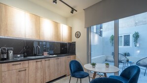 A modern kitchen with wooden cabinets, a black countertop, and a round table with blue chairs. - Luxury Studio w/ Backyard Near Plaka & Acropolis 3 (Athens)