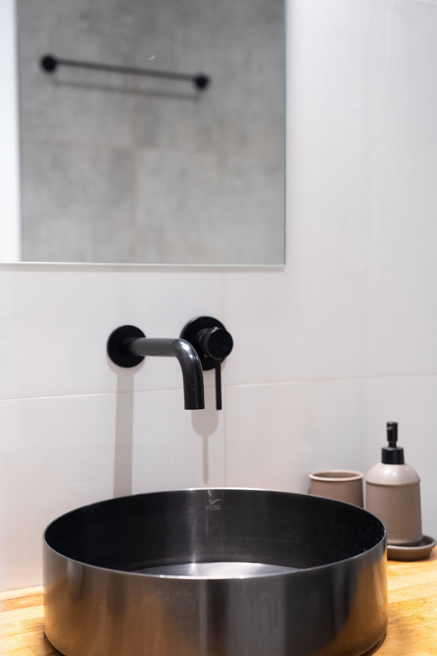 Un évier en acier inoxydable avec un robinet noir, un miroir au-dessus et un plan de travail en bois.