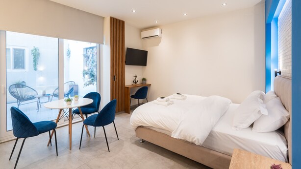 A modern hotel room with a large bed, a desk with a chair, a TV, and a balcony with chairs and a table. - Luxury Studio w/ Backyard Near Plaka & Acropolis 3 (Athens)