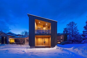 A modern two-story house with a wooden facade and a balcony, surrounded by snow. - Chalet Opus (Hakuba)