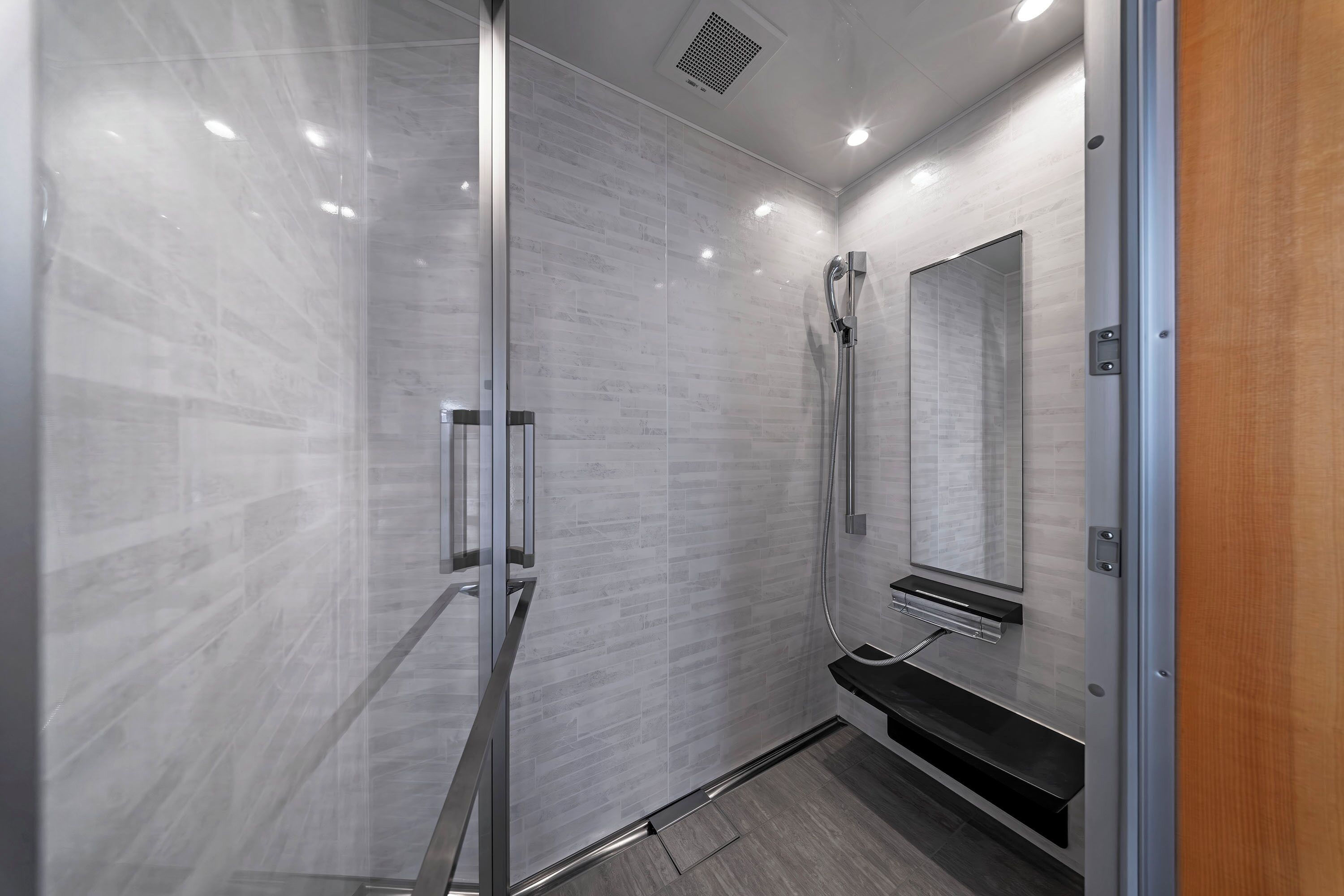 A modern bathroom with a glass shower enclosure, a large mirror, and a wooden vanity.