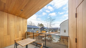 A balcony with wooden flooring, a table, two chairs, and a glass railing. - Chalet Opus (Hakuba)