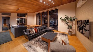 A modern living room with a wooden ceiling, a black leather sofa, a dining area, and large windows. - Chalet Opus (Hakuba)