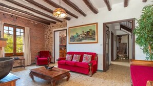 A room with exposed wooden beams, a red sofa, a painting, and a staircase leading to another level. - Holiday Home 'Can Garriga, Casa Principal' with Mountain View, Private Terrace and Wi-Fi (Girona)