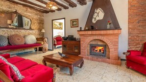 A cozy living room with a brick fireplace, red sofas, and a wooden coffee table. - Holiday Home 'Can Garriga, Casa Principal' with Mountain View, Private Terrace and Wi-Fi (Girona)