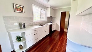 A modern kitchen with white cabinetry, a stainless steel kettle, a sink, and a window with a view.