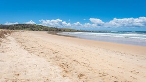 A sandy beach with gentle waves, a clear sky, and a distant shoreline with vegetation.