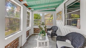 A sunroom with a rustic ceiling, large windows, wicker furniture, and a glass table. - Young Street Homes (Panama City Beach)