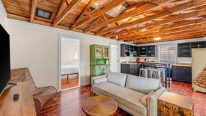 A spacious living area with a high wooden ceiling, a sofa, a wicker table, and a kitchen in the background. - Young Street Homes (Panama City Beach)