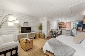 A cozy room with a bed, a TV, a dining table, and a kitchen area. - Young Street Homes (Panama City Beach)