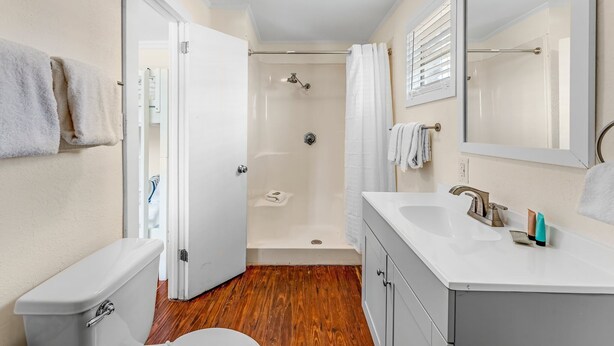 A bathroom with a shower, toilet, sink, and a mirror. - Young Street Homes (Panama City Beach)