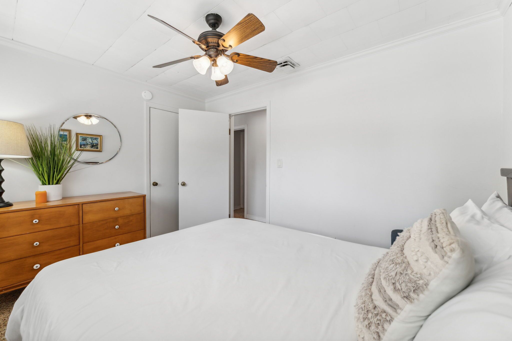 A bedroom with a bed, a wooden dresser, a ceiling fan, and a door leading to another room.